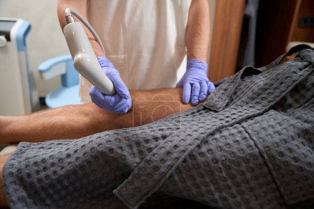 Foto de Cropped photo of medical staff using shockwave therapy for helping patient live with less pain - Imagen libre de derechos