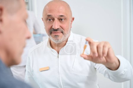 Photo for Elderly doctor communicates with a patient in a medical center, he demonstrates an ampoule with medicine - Royalty Free Image