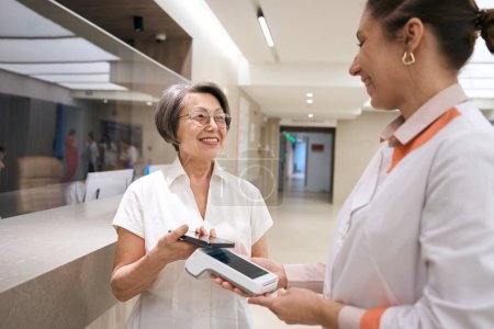 Photo for Patient pays for her visit to the therapist, the medical worker holds the terminal - Royalty Free Image