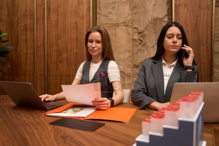 Téléchargez les photos : Young female colleagues work at a large table in a stylish office, they use a phone, a laptop - en image libre de droit
