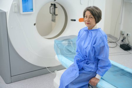 Foto de Calm elderly woman sits in the CT room before the diagnostic procedure, modern equipment indoors - Imagen libre de derechos