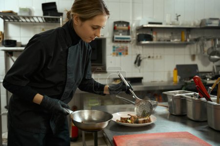 Foto de Joven cocinera en una cocina profesional pone carne en un plato, ella cocinó la carne sous vide - Imagen libre de derechos