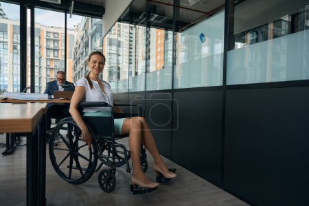 Téléchargez les photos : Woman with beautiful legs sits in a wheelchair, her colleague works at a computer - en image libre de droit