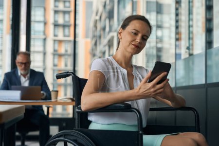 Téléchargez les photos : Femme d'affaires en fauteuil roulant bavarde au téléphone, son employé travaille à la table - en image libre de droit