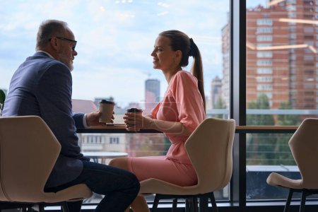 Téléchargez les photos : Employees of a business company, a woman and a man, communicate over a cup of coffee during a break. - en image libre de droit