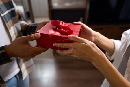 Foto de Hermosa caja de regalo roja en las manos de una pareja enamorada, la caja está atada con una cinta roja - Imagen libre de derechos