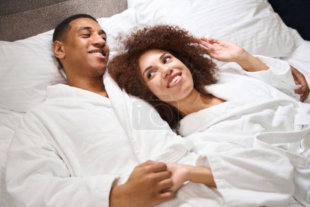 Téléchargez les photos : Mignonne femme multiraciale repose sur l'épaule de son mari, le couple s'est installé sur un lit confortable - en image libre de droit