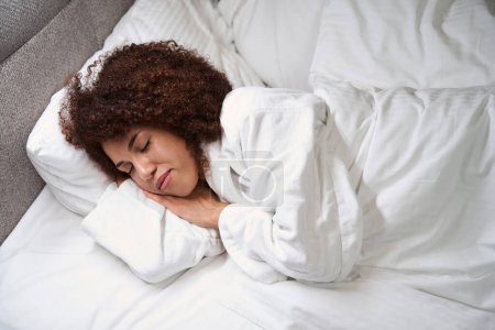 Foto de Linda mujer joven rizada duerme en la cama con las manos debajo de la mejilla, tiene una hermosa piel oscura - Imagen libre de derechos
