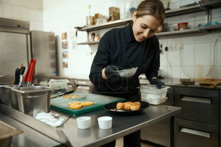Téléchargez les photos : Satisfied chef sprinkles syrniki with powdered sugar, modern equipment indoors - en image libre de droit