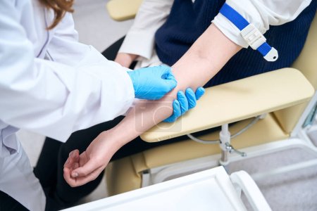 Asistente de laboratorio inserta una aguja en la vena del paciente, el trabajador de la salud utiliza guantes de protección