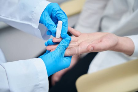 Téléchargez les photos : Assistant de laboratoire fait une perforation du doigt pour l'échantillonnage du sang, l'agent de santé utilise une aiguille spéciale - en image libre de droit