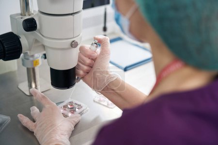 Foto de Embriólogo examina el biomaterial recogido en bloques de embriones bajo un potente microscopio, el especialista utiliza una jeringa especial - Imagen libre de derechos