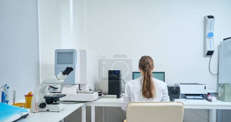 Photo for Woman works at a computer in a diagnostic laboratory, there is a lot of special equipment in the room - Royalty Free Image