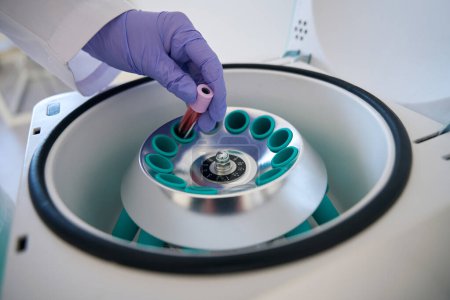 Téléchargez les photos : Assistant de laboratoire dans un laboratoire de diagnostic met un tube à essai avec un échantillon de sang dans une centrifugeuse hématologique - en image libre de droit