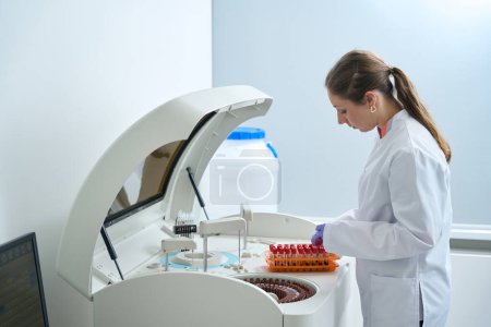 Téléchargez les photos : Femme effectue des diagnostics de laboratoire dans l'unité de test, elle utilise un analyseur biochimique moderne - en image libre de droit