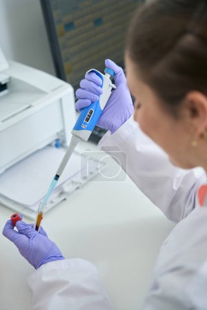 Téléchargez les photos : Femme recueille des biomatériaux à partir d'un tube à essai avec un distributeur spécial, à côté de l'équipement moderne - en image libre de droit