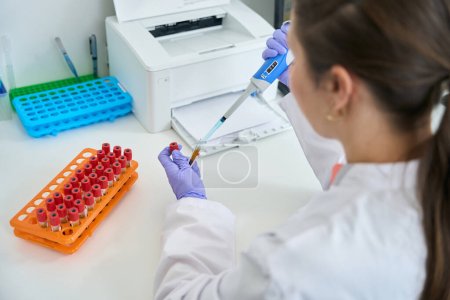 Laborantin arbeitet mit Blutproben, die in Reagenzgläser geladen werden, Reagenzgläser werden in einem Block gesammelt