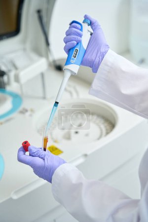 Téléchargez les photos : L'assistant de laboratoire recueille les biomatériaux d'un tube à essai avec une pipette spéciale, l'équipement est dans l'unité d'essai - en image libre de droit