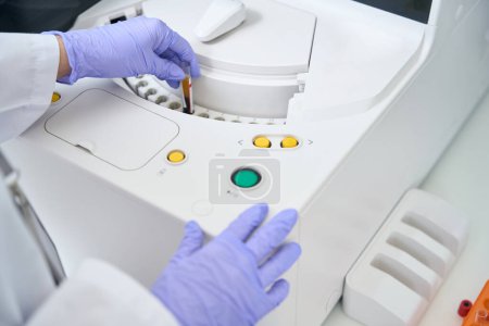 Téléchargez les photos : Assistant de laboratoire met une éprouvette avec un échantillon de sang dans un analyseur immunochimiluminescent, c'est un appareil de diagnostic moderne - en image libre de droit