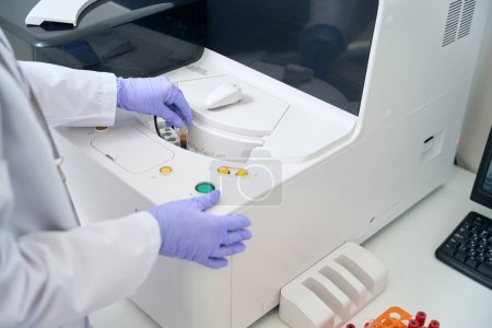 Téléchargez les photos : Un assistant de laboratoire retire une éprouvette avec un échantillon de sang d'un analyseur hématologique, c'est un appareil de diagnostic moderne - en image libre de droit