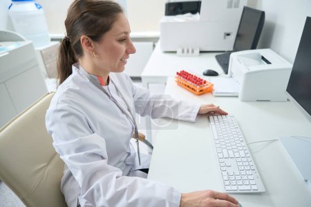 Photo for Smiling woman making a printout of the results of the hematology analyzer in the testing unit - Royalty Free Image