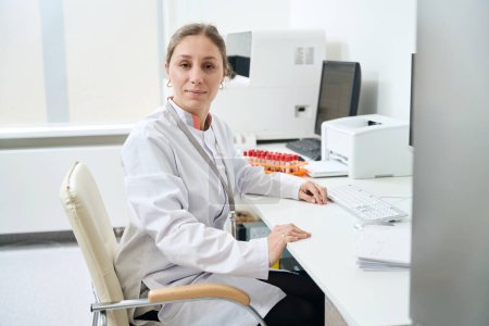 Photo for Laboratory employee is sitting at her desk, she is in the testing unit in the testing unit - Royalty Free Image