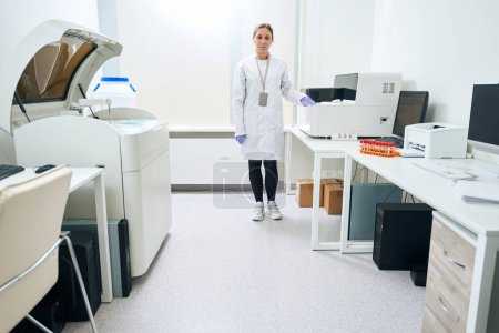 Téléchargez les photos : Une travailleuse de la santé se tient debout dans l'unité de test, il y a beaucoup d'ordinateurs et d'analyseurs d'hématologie dans la pièce - en image libre de droit