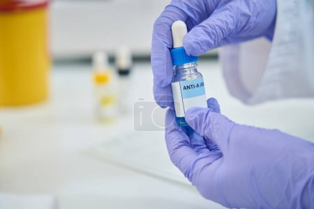 Photo for Reagent for determining blood type in hands of laboratory employee, this is liquid in a bottle with a blue cap - Royalty Free Image