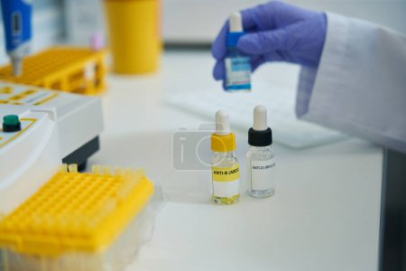 Photo for Laboratory assistant in protective gloves holds reagent for determining blood type, on laboratory table there are test tubes in blocks - Royalty Free Image