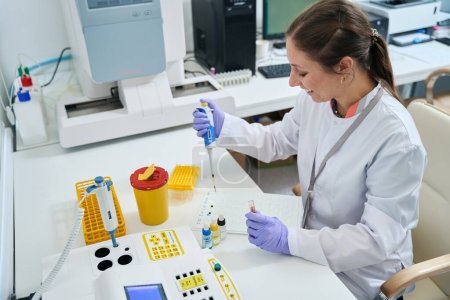 Foto de Asistente de laboratorio femenino realiza una prueba de grupo sanguíneo en la unidad de prueba, el laboratorio está equipado con equipos modernos - Imagen libre de derechos
