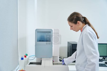 Photo for Hematologist launches an immunochemiluminescent analyzer, a woman in overalls and protective gloves - Royalty Free Image