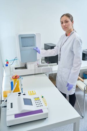 Foto de Trabajador de la salud enciende el analizador de hematología, el laboratorio moderno está equipado con equipos de diagnóstico - Imagen libre de derechos