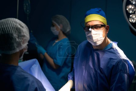 Photo for Doctor with an operating room nurse and assistants at the workplace in the operating room, personnel in protective masks - Royalty Free Image