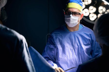 Photo for Experienced surgeon with assistants at the workplace in the operating room, staff in surgical overalls - Royalty Free Image