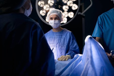Foto de Una cirujana está en el quirófano en la mesa de operaciones, el médico tiene un bisturí en las manos. - Imagen libre de derechos