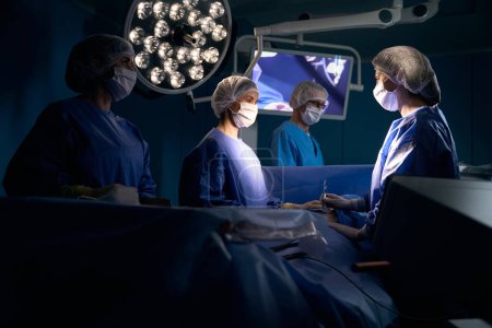 Foto de El hombre bajo anestesia yace en la mesa de operaciones, es operado por un equipo quirúrgico - Imagen libre de derechos