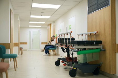 Foto de Las personas con ropa casual están sentadas en un pasillo del hospital, en primer plano hay una cama móvil - Imagen libre de derechos