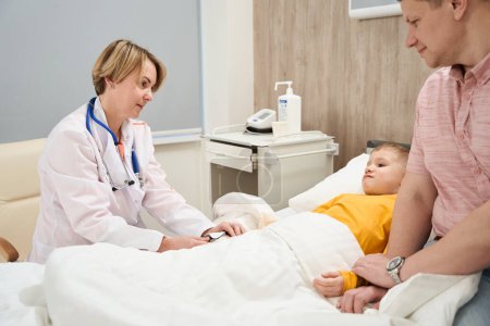 Photo for Waist up side view portrait of elegant qualified pediatrician is talking with child in the medical ward - Royalty Free Image