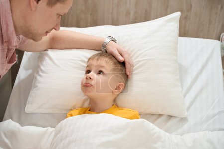Téléchargez les photos : Gros plan portrait de petit garçon nerveux sur le lit médical en regardant son père à l'hôpital - en image libre de droit