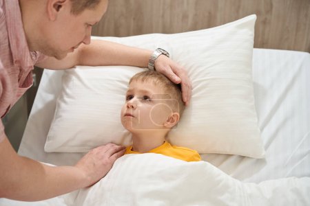 Foto de De cerca retrato de niño deprimido está acostado en la cama médica mientras mira a su padre en el cuarto de los enfermos - Imagen libre de derechos