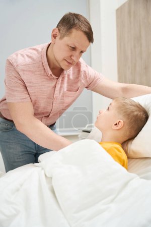 Foto de De cerca el retrato del guapo padre caucásico está hablando con su hijo en el cuarto de los enfermos - Imagen libre de derechos
