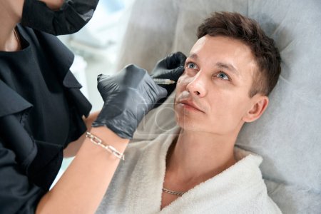 Téléchargez les photos : Cosmetologue dans des gants de protection tenant la seringue et faisant des injections de beauté pour le visage à l'homme - en image libre de droit