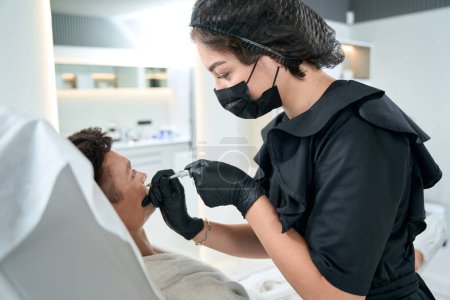 Téléchargez les photos : Femme dans des gants de protection tenant la seringue et faisant des injections de beauté pour le visage à l'homme - en image libre de droit