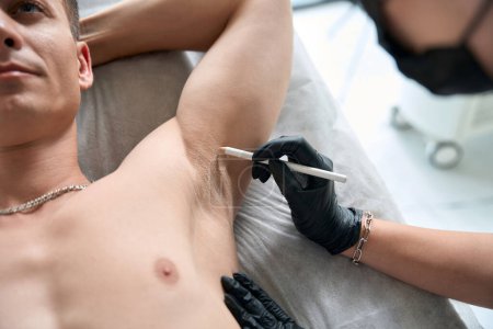 Téléchargez les photos : Dermatologue dans des gants de protection tenant la seringue et faisant des injections de beauté dans l'aisselle à l'homme - en image libre de droit