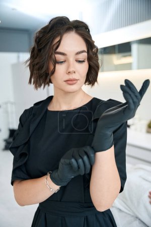 Téléchargez les photos : Portrait de jolie cosmétologue en manteau médical debout dans le bureau et prêt pour le travail - en image libre de droit