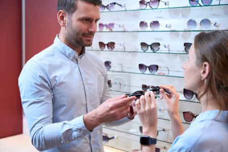Photo for Waist up portrait of bearded qualified optician is presenting new foreign collection of eyeglasses in the luxury store - Royalty Free Image