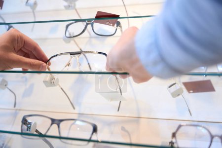 Téléchargez les photos : Portrait à angle bas d'une personne non reconnue choisit les lunettes de vue élégantes pour le moment dans le magasin d'optique - en image libre de droit