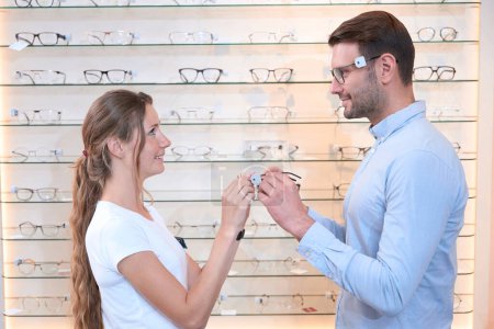 Photo for Waist up side view portrait of lovely couple is visiting the optician shop while woman is helping to man to make his eyes look perfect - Royalty Free Image