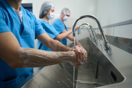 Téléchargez les photos : Une équipe de chirurgiens se lave soigneusement les mains, les médecins et les infirmières en uniforme chirurgical se préparent pour l'opération - en image libre de droit