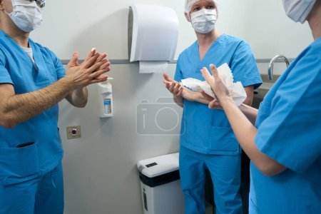 Téléchargez les photos : Groupe de travailleurs médicaux dans des masques de protection traite leurs mains avec un désinfectant, les médecins en salopette - en image libre de droit